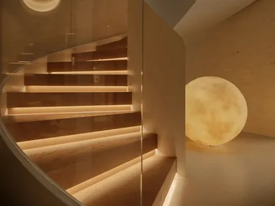 Modern curved wooden staircase with integrated LED lighting, glass railing, textured concrete walls, and two large spherical moon lamps providing soft illumination.
