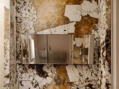 Modern bathroom featuring a double vanity carved from Calacatta marble with bold bronze and brown veining, paired with a floating stainless steel cabinet and a large frameless mirror.