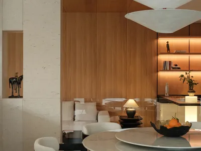 Modern luxury dining room featuring a round travertine marble table, black-framed upholstered chairs, curved ceiling detail, and warm wooden built-in cabinetry with integrated lighting.