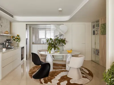 Modern dining area featuring a round Calacatta marble table, black Panton chair, cream boucle chairs, and a brown-and-white cowhide rug in a bright open-plan kitchen and living space.
