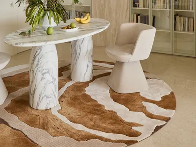 Modern dining area featuring a round Calacatta marble table on sculptural bases, a cream bouclé swivel chair, a large white pendant lamp, and floor-to-ceiling built-in bookshelves with light wood paneling.