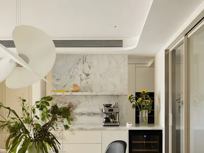 Modern open kitchen and dining area with Calacatta marble round table, black organic-shaped chair, beige bouclé armchair, and marble backsplash with built-in coffee station.