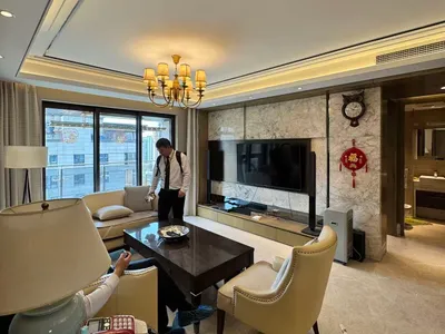 現代奢華客廳，設有米色皮革沙發、深木茶几、大理石電視牆、水晶吊燈，以及可眺望城市建築的大窗。
