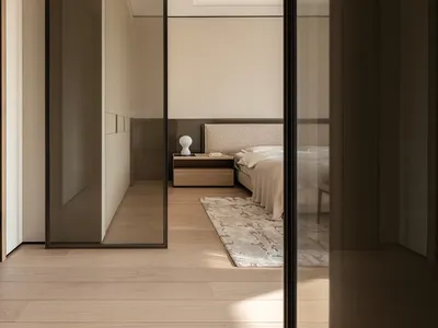 現代簡約臥室一景，淺色橡木地板、中性米色牆面、織紋布質床頭板、懸浮式床頭櫃與抽象圖案地毯。