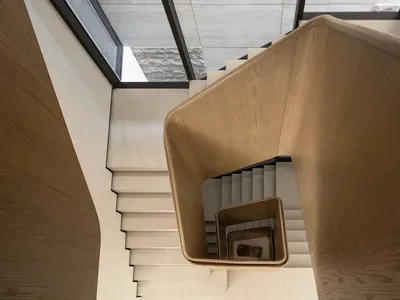Top-down view of a modern curved oak staircase with continuous wooden handrail and floating light-colored steps in a minimalist interior.