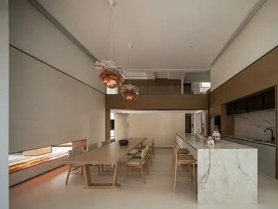 現代雙層挑高開放式廚房與餐廳，包含淺橡木長餐桌、大理石中島，以及兩盞大型木質藝術吊燈。