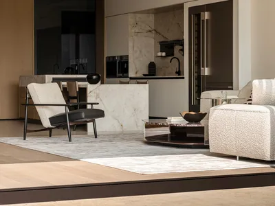 Modern minimalist living room featuring a white marble kitchen island, boucle sofa, black leather and wood armchair, and integrated stainless steel appliances.