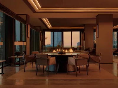 Modern luxury dining room featuring a large round walnut dining table with six upholstered chairs, warm cove lighting, and floor-to-ceiling windows showing a city skyline at sunset with a fireplace in the background.
