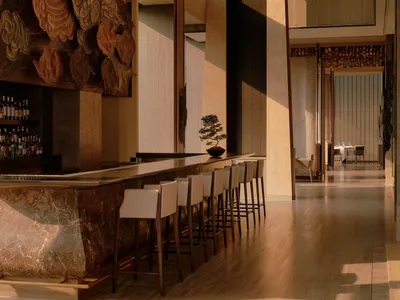 Luxurious long marble bar with white leather bar stools in a high-end lounge featuring a massive traditional Chinese cloud pattern wall carving and warm ambient lighting.