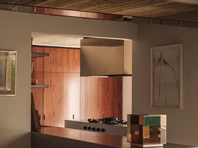 Modern minimalist kitchen featuring a concrete island, warm walnut wood cabinetry, wood-paneled ceiling, and sculptural boucle dining chairs.