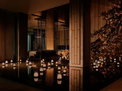 Luxurious Japanese restaurant interior featuring a shallow reflective water pool lined with glowing woven lanterns, dramatic dark wood architecture, and a large sculptural tree with golden leaves.