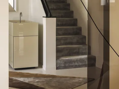 Modern minimalist entryway featuring a floating dark velvet carpeted staircase with a bold black handrail, paired with a glossy cream vanity and geometric rug.