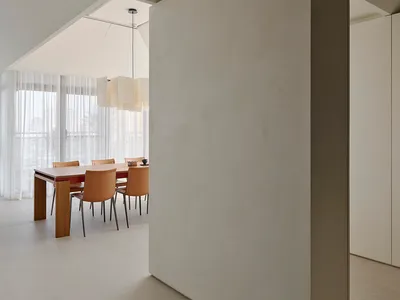 現代極簡風格餐廳，設有大型微水泥隔間半牆、木製餐桌、棕褐色皮革餐椅，以及高斜天花板下的大型雕塑感吊燈。