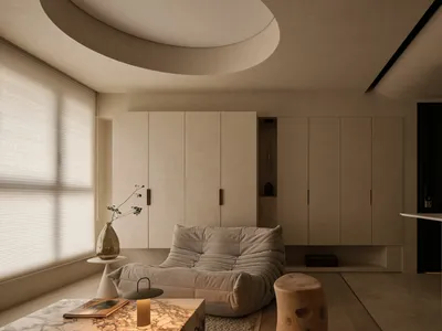 Modern minimalist living room featuring a Togo-style modular sofa, micro-cement walls and ceiling with a large circular recessed light, marble coffee table, and natural wood elements.