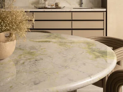Modern dining room with round Calacatta green marble table, beige curved dining chairs, and a luxurious marble wet bar with amber textured glass upper cabinets and under-cabinet lighting.