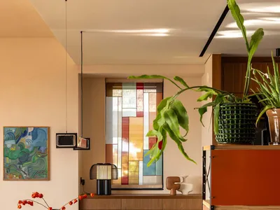 Modern dining room featuring a walnut sideboard, cane-backed folding chairs, a large stained-glass window, and warm neutral walls with wooden flooring.