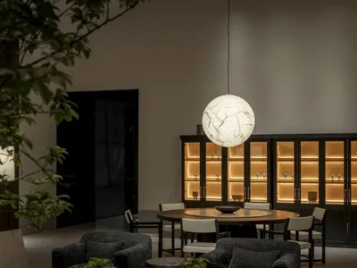 Modern luxury living and dining area featuring dark boucle swivel armchairs, a large spherical pendant lamp, round wooden dining table, and illuminated dark wood display cabinets.