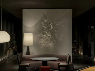 Luxurious modern game lounge featuring a curved textured sofa, round black table, dramatic tree shadow projection on a backlit wall, and warm ambient lighting.
