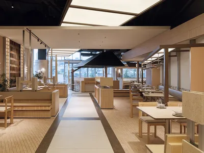 Modern Japanese restaurant interior featuring light wood banquette seating, stone-topped tables, and a long central aisle with skylight illumination.