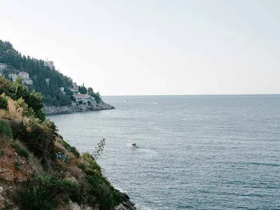 Luxurious wooden terrace with teak lounge chairs overlooking a rocky Mediterranean coastline and deep blue sea.