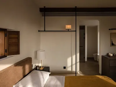 Modern minimalist bedroom with brown upholstered bed, mustard yellow throw, walnut furniture, and black sliding door leading to an ensuite bathroom