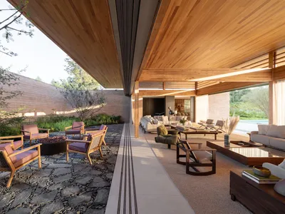 Modern covered outdoor living area featuring a stone-paved courtyard with fire pit, wooden lounge chairs with pink cushions, and a spacious open-plan interior lounge with warm wood ceilings and neutral furnishings.