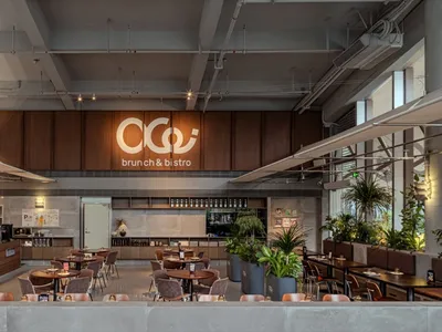 現代工業風早午餐與小酒館室內空間，溫潤胡桃木板牆、混凝土元素、軟墊座椅與大量盆栽植物，在明亮自然光與人工照明下。