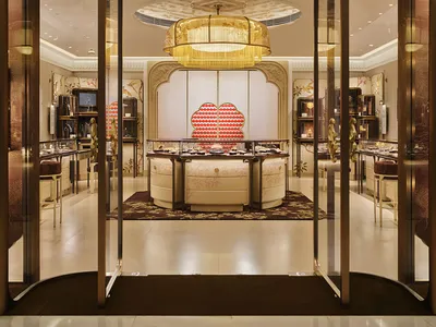 Luxurious jewelry store interior with a large golden woven lantern chandelier, curved cream display counters, ornate wall panels, and glass entrance doors.