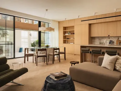 Modern open-plan living room featuring light oak cabinetry, white marble dining table, dark green velvet lounge chair, and a large L-shaped sectional sofa in neutral tones.