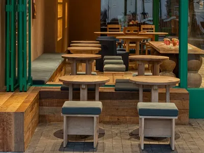 Modern cafe interior featuring round oak stools, built-in wooden banquettes with green cushions, and a bold emerald green entrance frame.