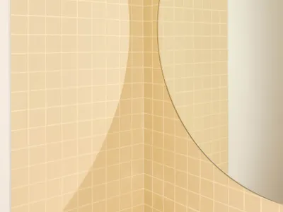 Close-up view of a bathroom corner featuring butter yellow square ceramic tiles, white grout, and a large round mirror with a thin gold frame.