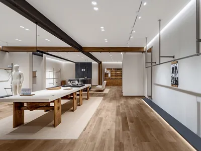 簡約家具展示間長景，設有大型橡木與水泥展示桌、淺色木地板、 recessed 天花燈光與木樑。