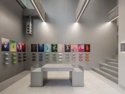 Modern minimalist sneaker retail store interior with raw concrete walls, linear LED lighting, glass display table, and colorful sneaker wall display arranged in a grid.
