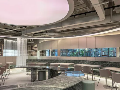 現代餐廳室內空間，設有長弧形綠色大理石吧台、配套圓凳、軟墊餐椅，以及巨型圓形粉色發光天花板裝置。