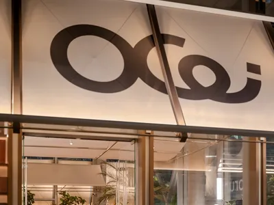 Ocoi餐廳夜間入口，玻璃門敞開，可見長型溫暖木質共享餐桌、豐富室內綠植與優雅現代燈光。