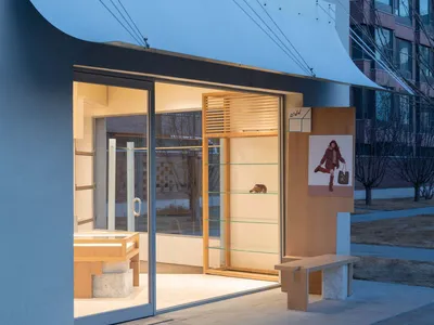 現代極簡風格精品店店面，暮色中可見發光橡木展示架、混凝土長椅與大面積玻璃入口。