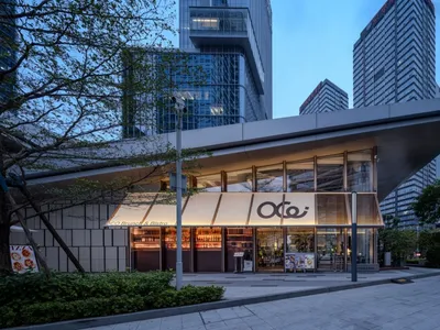OCO 早午餐酒館的現代玻璃與混凝土立面夜景，招牌與室內燈光溫暖明亮，周圍環繞著高樓大廈。