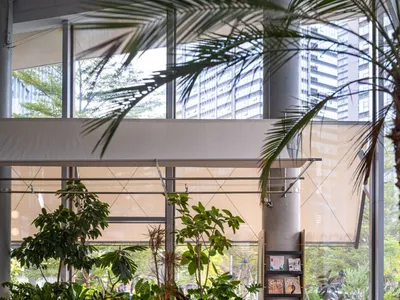 現代綠意餐廳室內空間，設有長型胡桃木共享餐桌、木長椅、球形吊燈、豐富室內植物，以及可眺望城市景觀的大片落地窗。