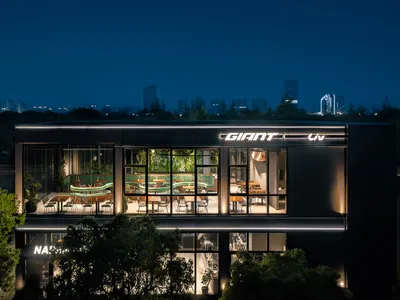夜間拍攝的兩層樓現代玻璃帷幕餐廳，室內可見弧形綠色沙發座、豐富植栽與明亮燈光，品牌為 Giant Liv。
