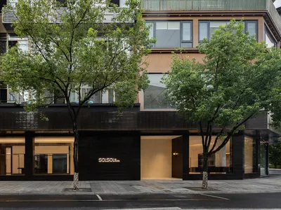SOLSO by SOLSO 零售店街景，現代黑色磁磚立面、大面積玻璃展示溫暖室內照明，前方有綠樹環繞。