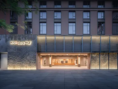 夜間拍攝的現代粗獷風商業建築入口，擁有質感混凝土牆面、發光金屬格柵屏風，以及亮著的RICHAUS招牌。