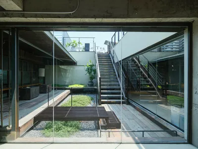 從現代混凝土住宅室內向外望去，陽光充足的中庭設有木甲板、碎石花園、盆栽植物與戶外樓梯。