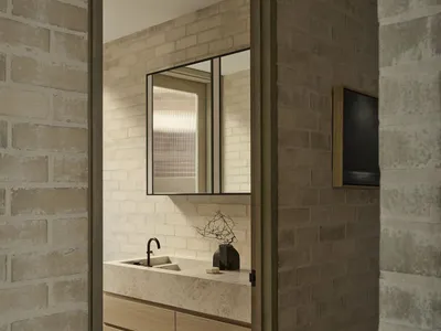 View into a modern brutalist bathroom with light travertine floating vanity, oak drawers, black matte faucet, and textured brick walls.