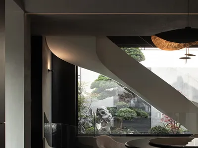 Modern minimalist dining area featuring a dramatic curved concrete wall, dark micro-cement floors, round dark dining table, textured bouclé chairs, and a large window overlooking a Japanese-inspired bonsai and rock garden.