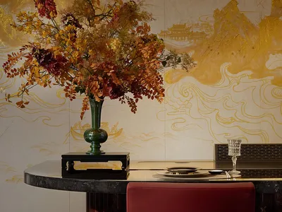圓形黑色大理石餐桌搭配紅絲絨餐椅，大型秋季花藝插花置於綠色花瓶中，背景為金色中國山水雲霧壁畫。