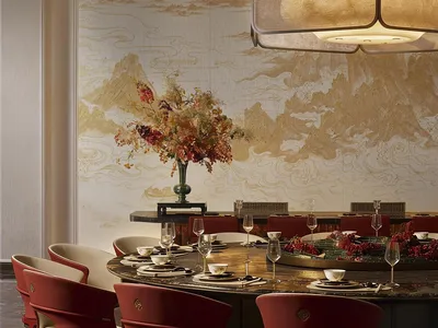Luxurious Chinese-style dining room featuring a large round marble table, red swivel armchairs with cream seats, a golden mountain-and-cloud mural on the wall, and a large fabric pendant light.