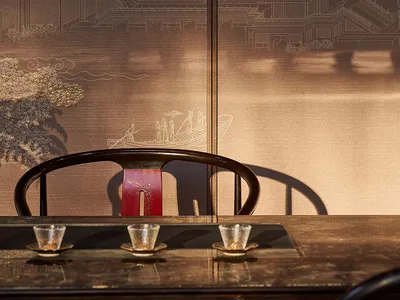 Dark rosewood horseshoe-back chair in front of a luxurious dark brown embroidered Chinese landscape screen featuring pavilions, mountains and river scenes, with three tea cups on a lacquered table.