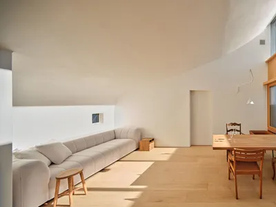 明亮的開放式客廳與餐廳，設有長型模組沙發、木製餐桌與經典木椅、弧形拱頂天花板，以及可見綠色磁磚戶外景觀的大窗。