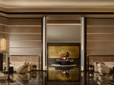Luxurious hotel lobby featuring high-gloss black marble floors, beige curved sofas, golden floral centerpiece, and backlit wood-paneled walls.