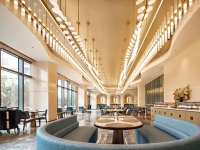 現代奢華飯店早餐廳，弧形藍色布面沙發、圓形大理石餐桌、戲劇性長型吊燈與拋光大理石地板。